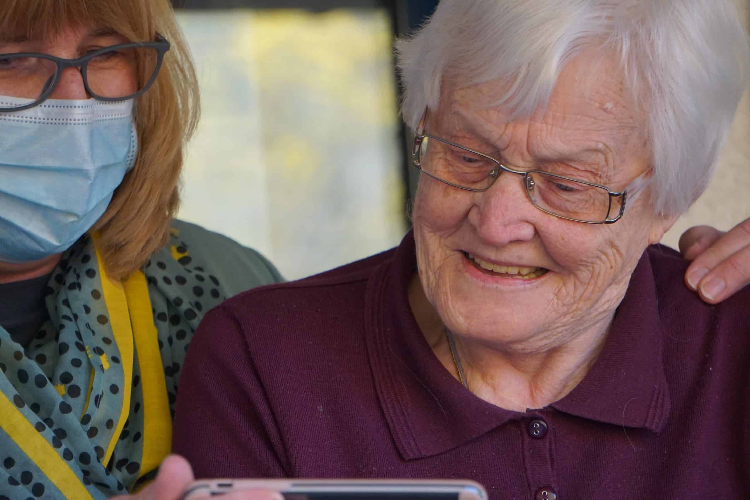 an older woman wearing a face mask looking at a cell phone.