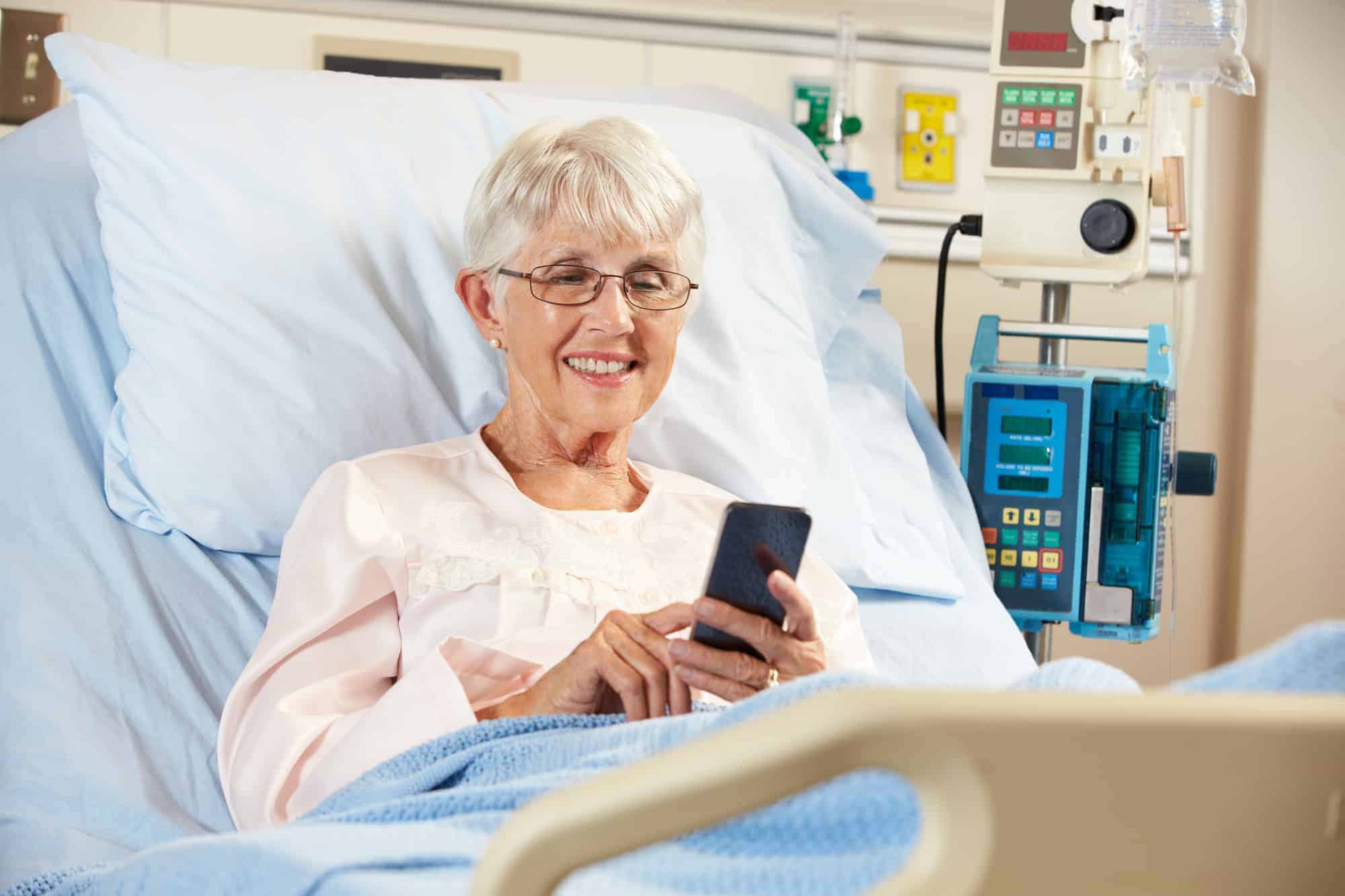 A patient using a cell phone on an adjustable hospital bed.