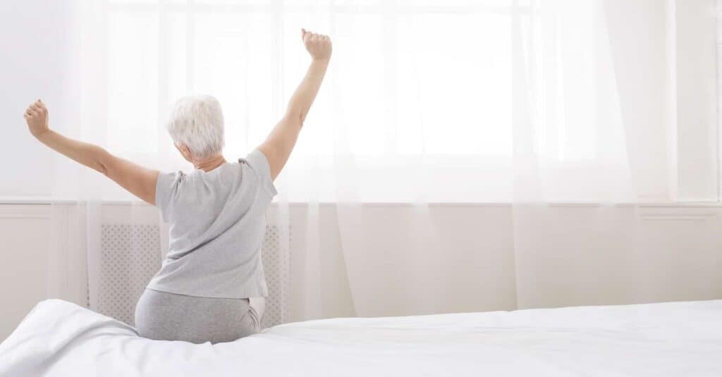 A woman raising her arms on a bed, contemplating hospital bed choices for home use.