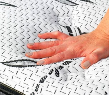 A person's hand is touching the top of a mattress.
