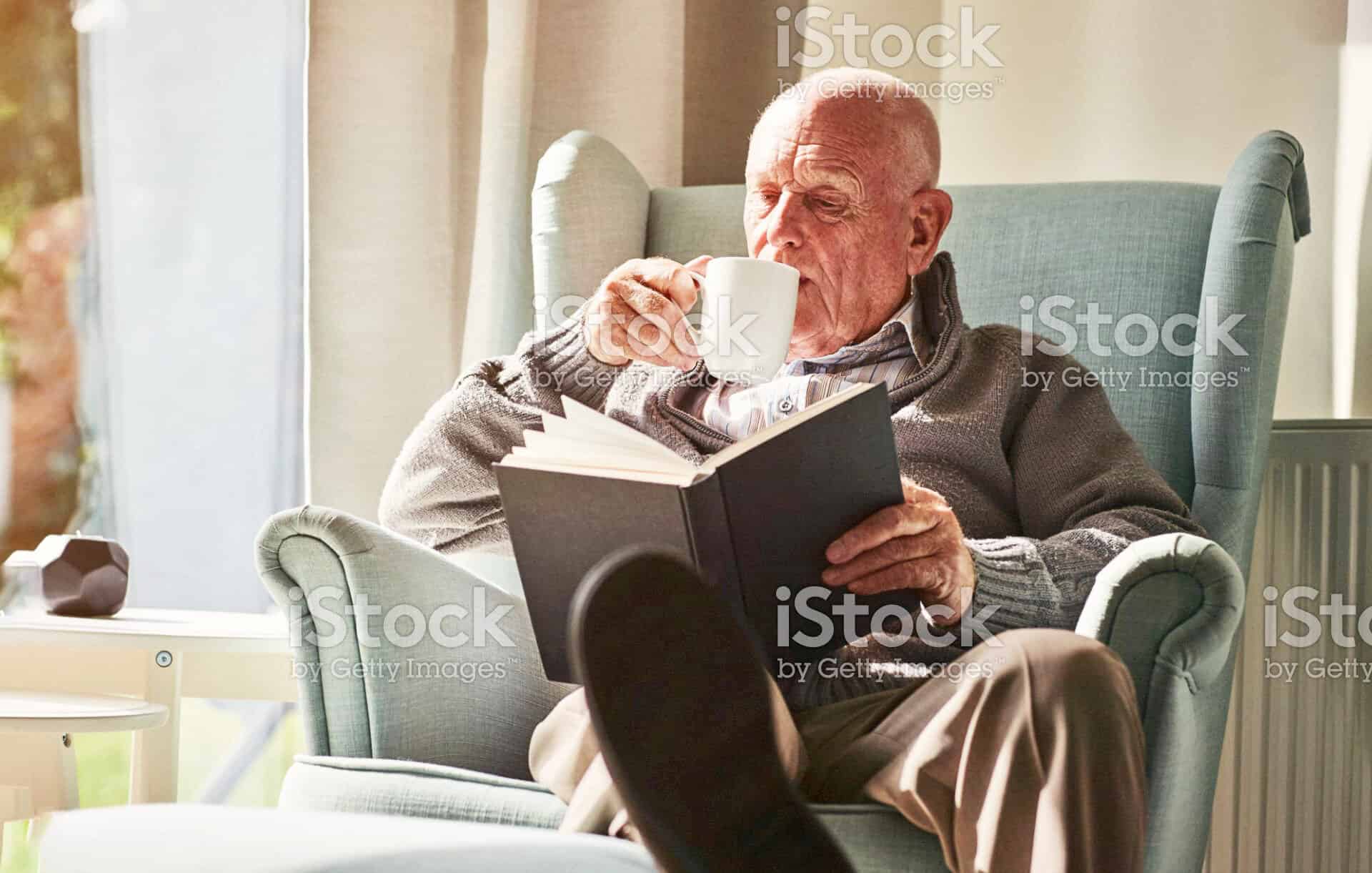 An elderly man sitting in a chair reading a book stock photo.