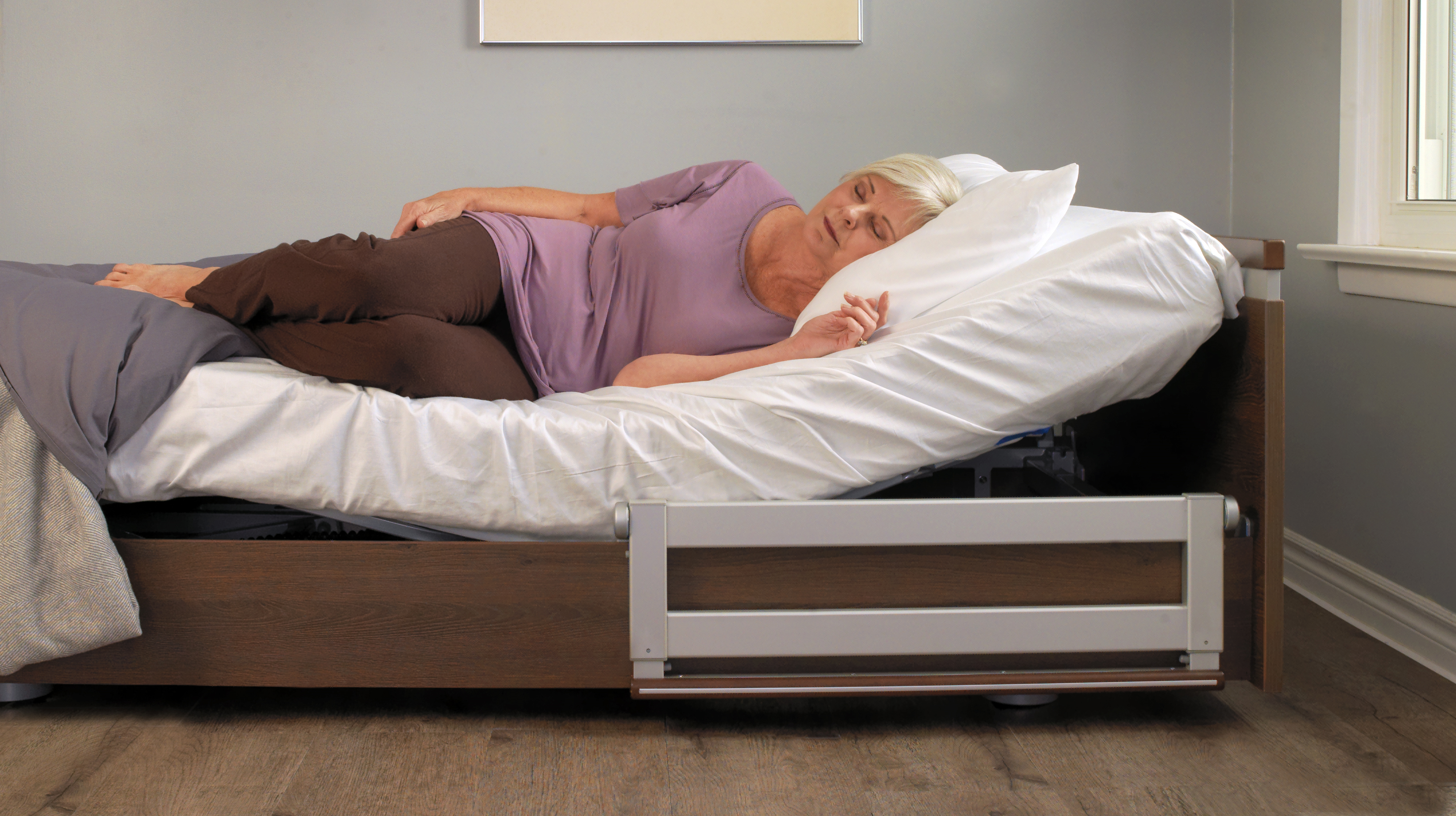 An elderly woman lying asleep in a hospital bed with an adjustable side rail in a calm room, captured in a Single Post on Elementor.