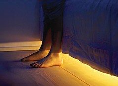 Feet touching the floor next to a bed, with soft yellow light glowing underneath.