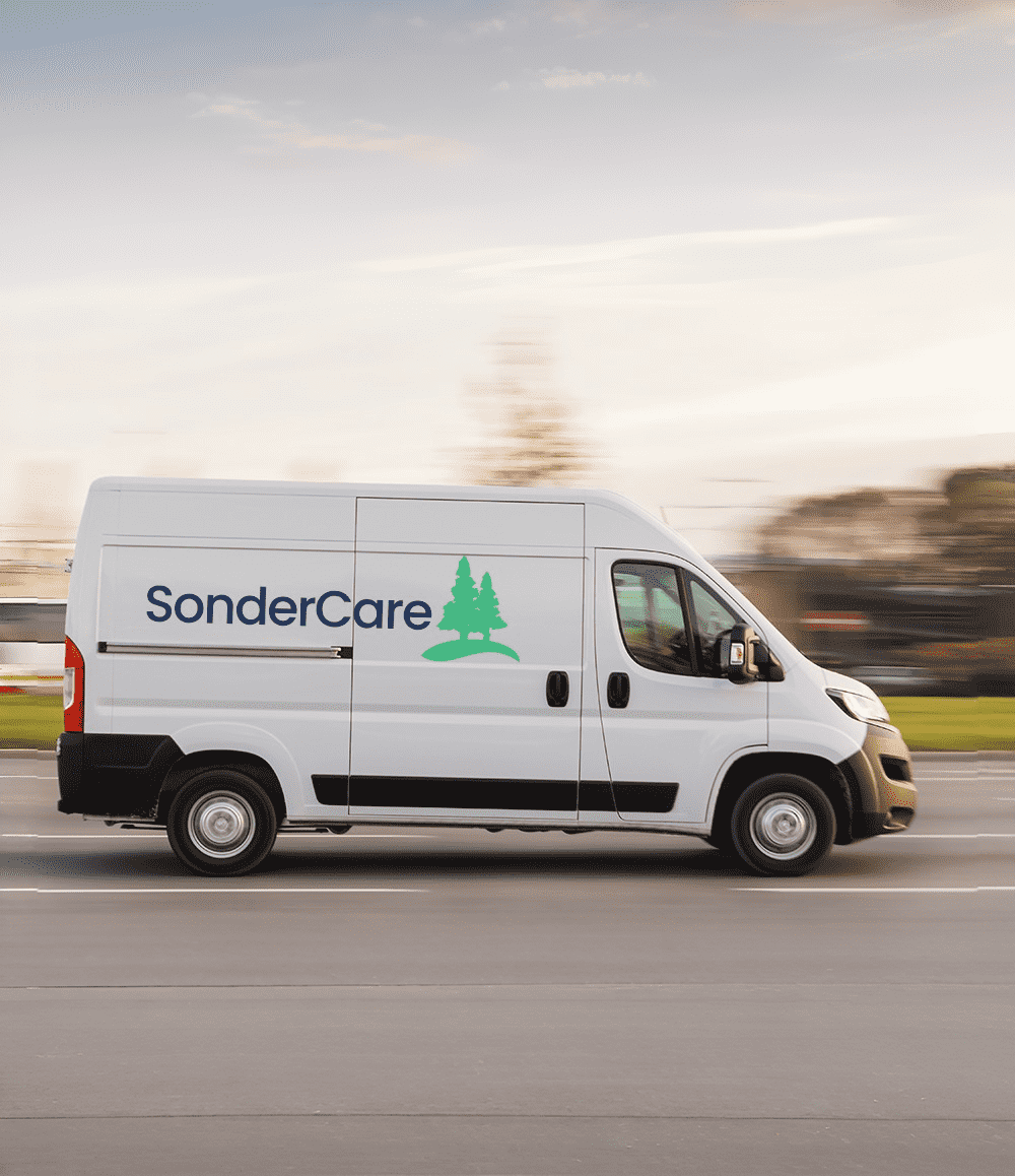 Delivery van with "SonderCare" branding, including a green tree logo, driving on a road with a blurred background.