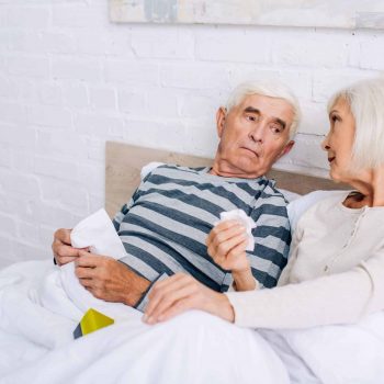 An elderly couple conversing in bed.