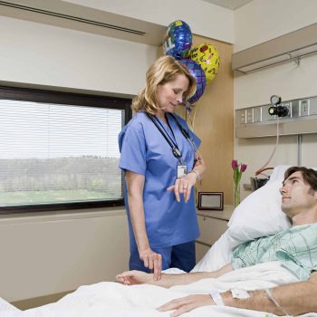 a woman standing next to a man in a hospital bed.