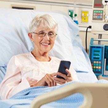 A patient using a cell phone on an adjustable hospital bed.